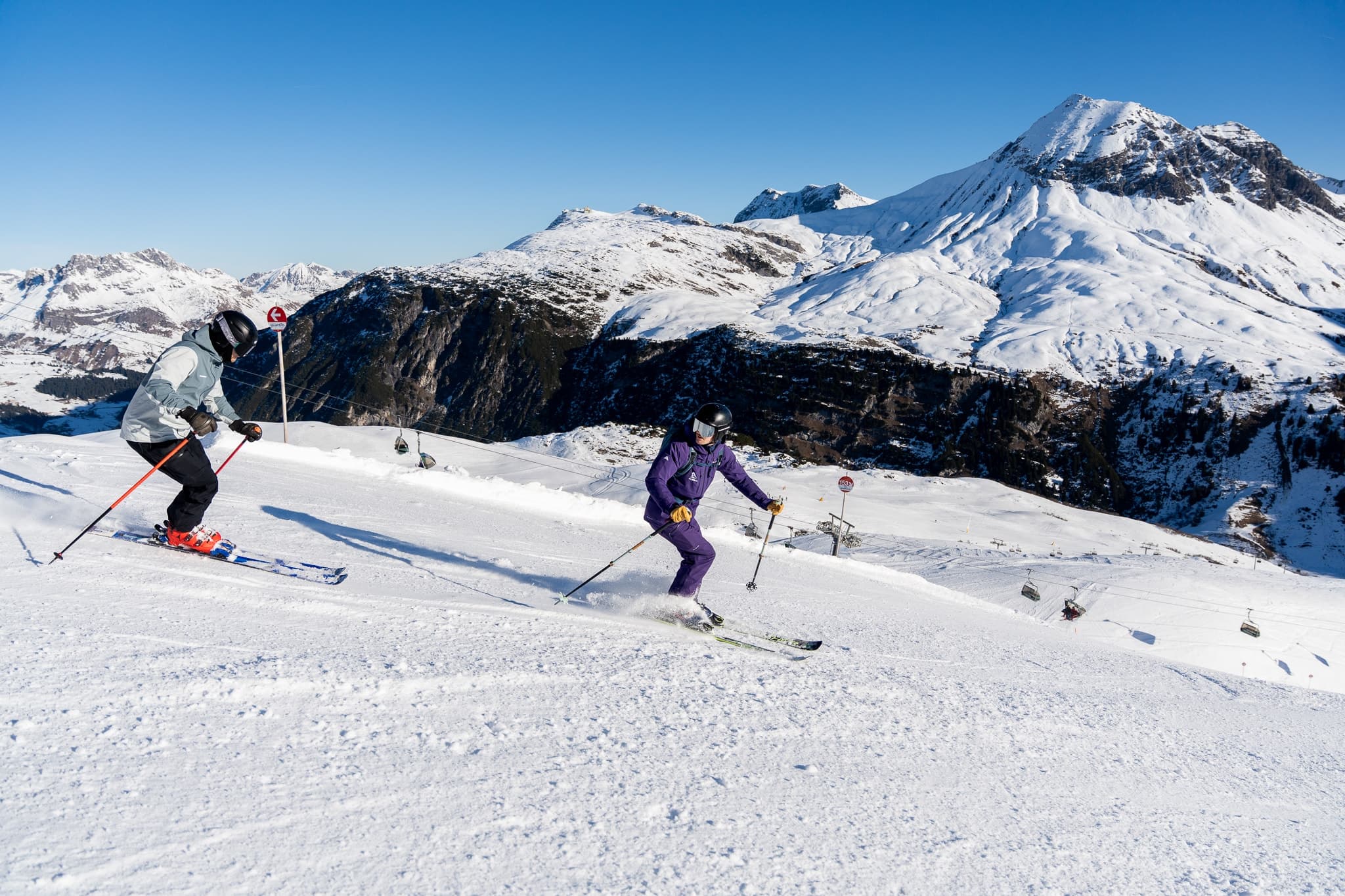 Two skiers carving down a groomed piste above Stuben am Arlberg.