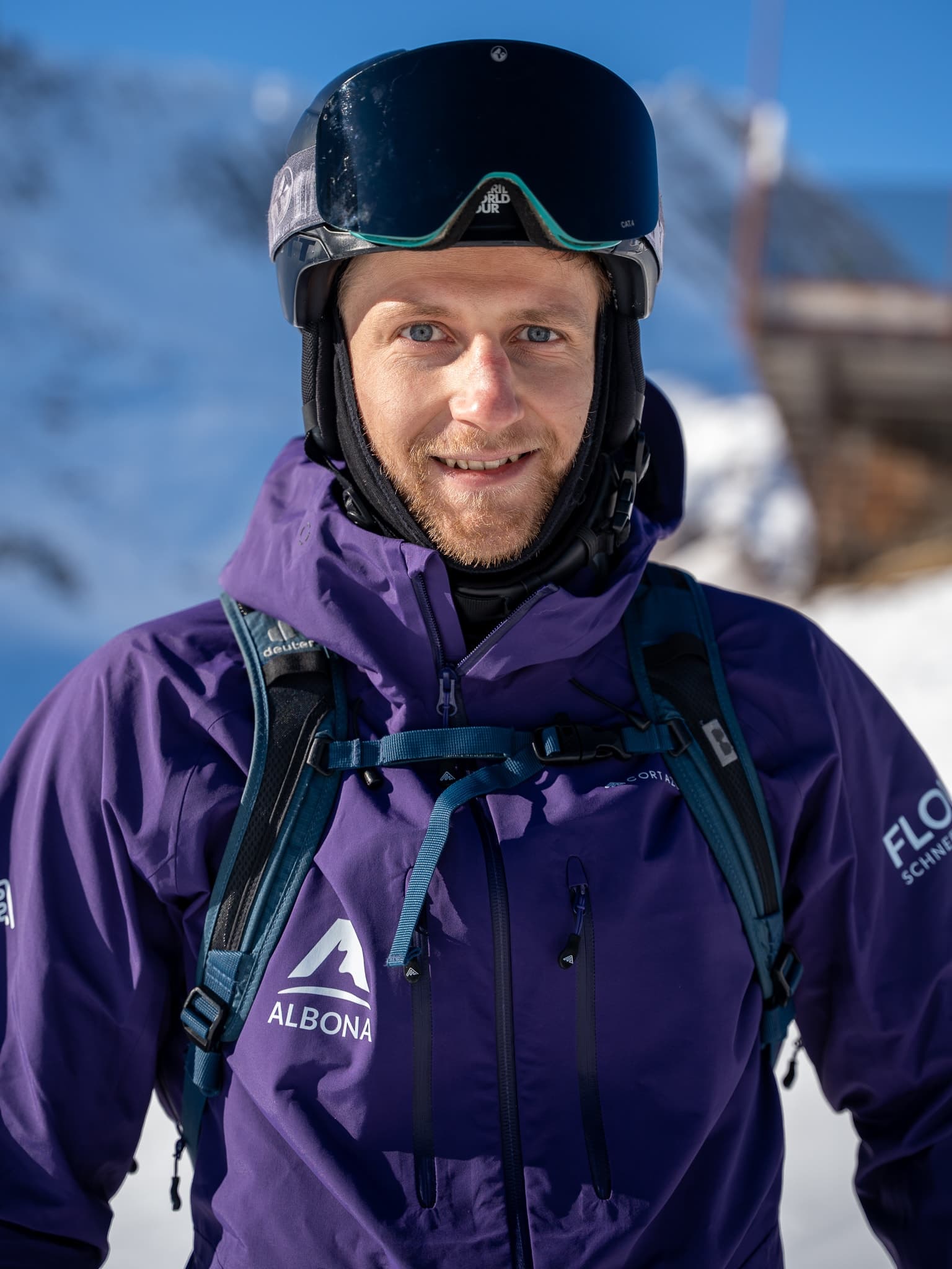 A flow guide in a purple Albona jacket smiles into the camera in front of a snowy Arlberg face.